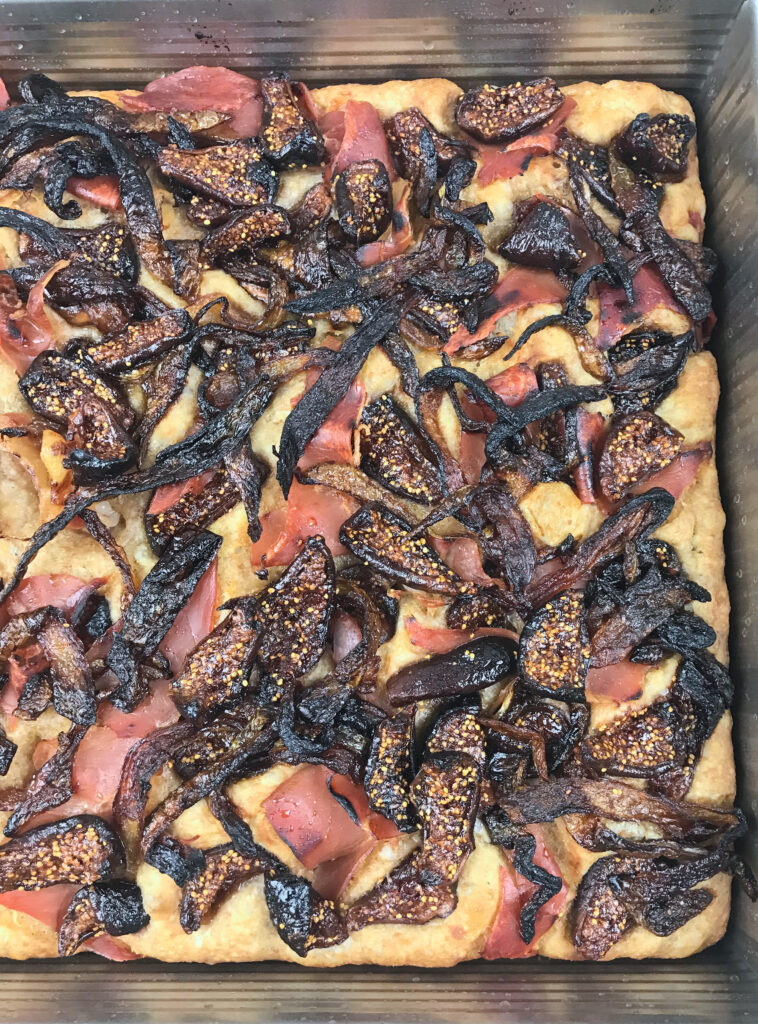 Fig yeast water focaccia topped with dried figs soaked in marsala, caramelized onions, salty prosciutto, and a touch of sea salt